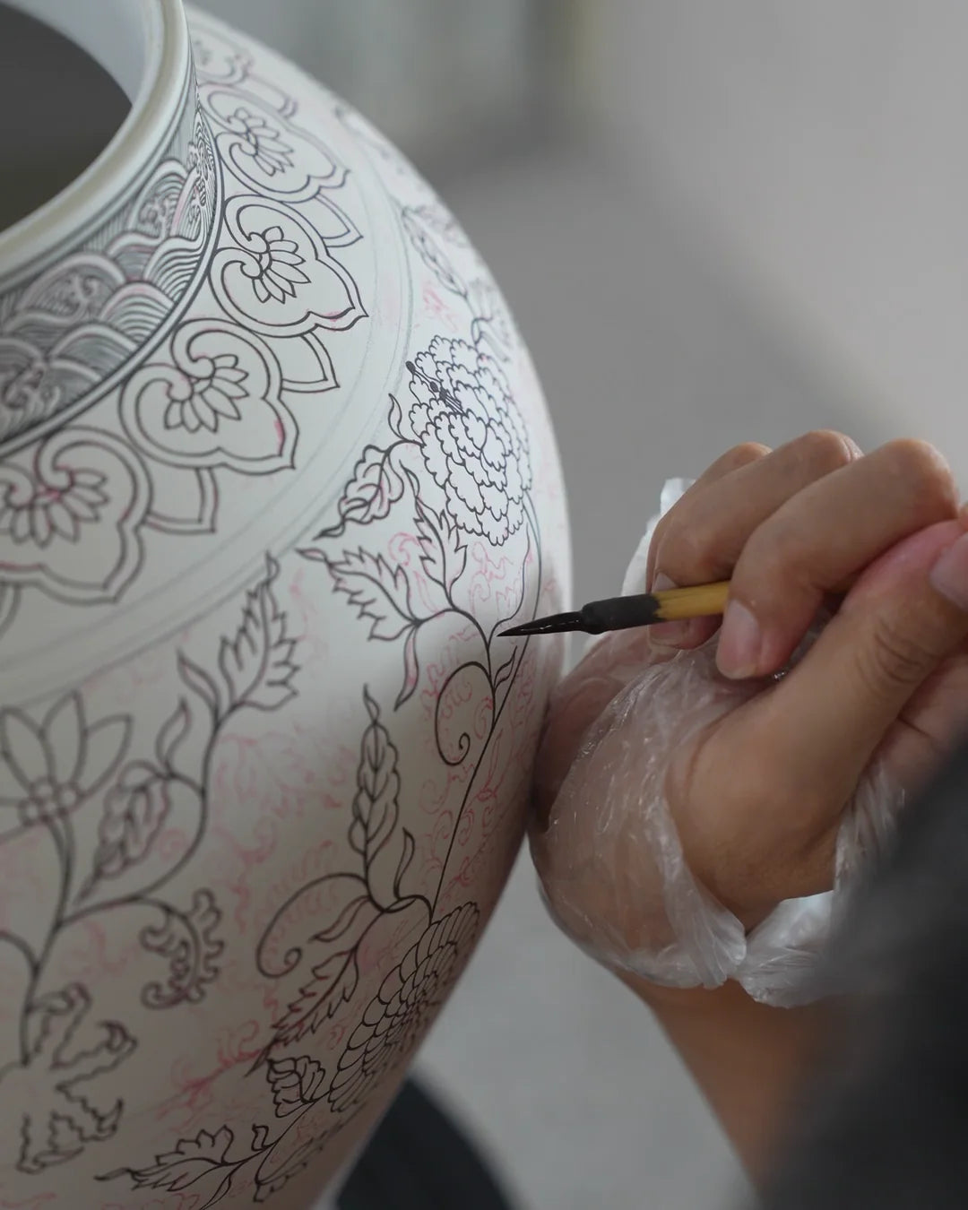 A craftsperson paints floral outlines onto a porcelain vessel